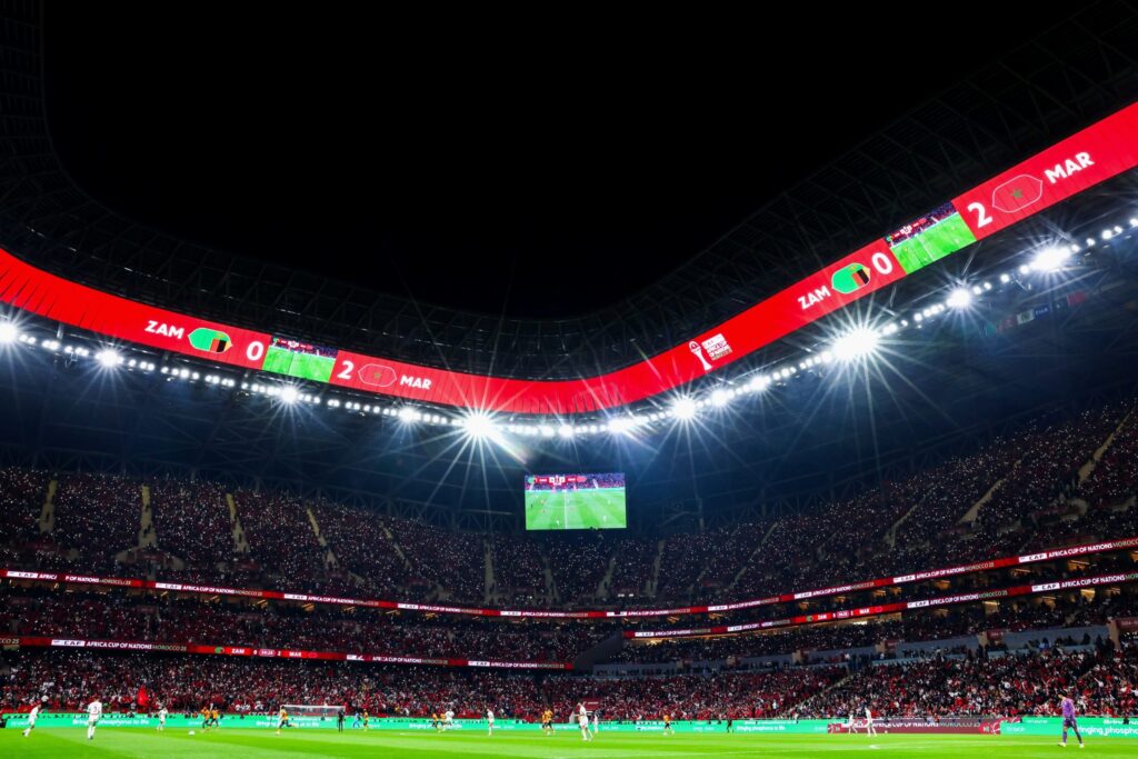 Stade de football éclairé pour la CAN 2025, symbole de l’économie du football africain, des droits médias et des influences institutionnelles